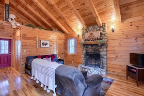 L’intérieur d’une cabane en rondins comprend un lit, un coin salon, une cheminée en pierre et un téléviseur.