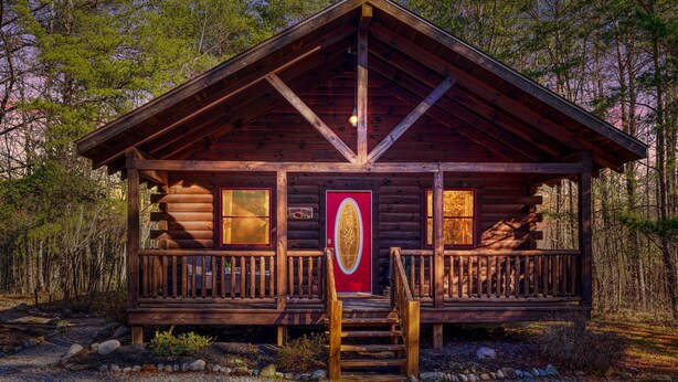 Eine Blockhütte mit einer Holzveranda, einer roten Tür und einer Treppe zum Eingang.