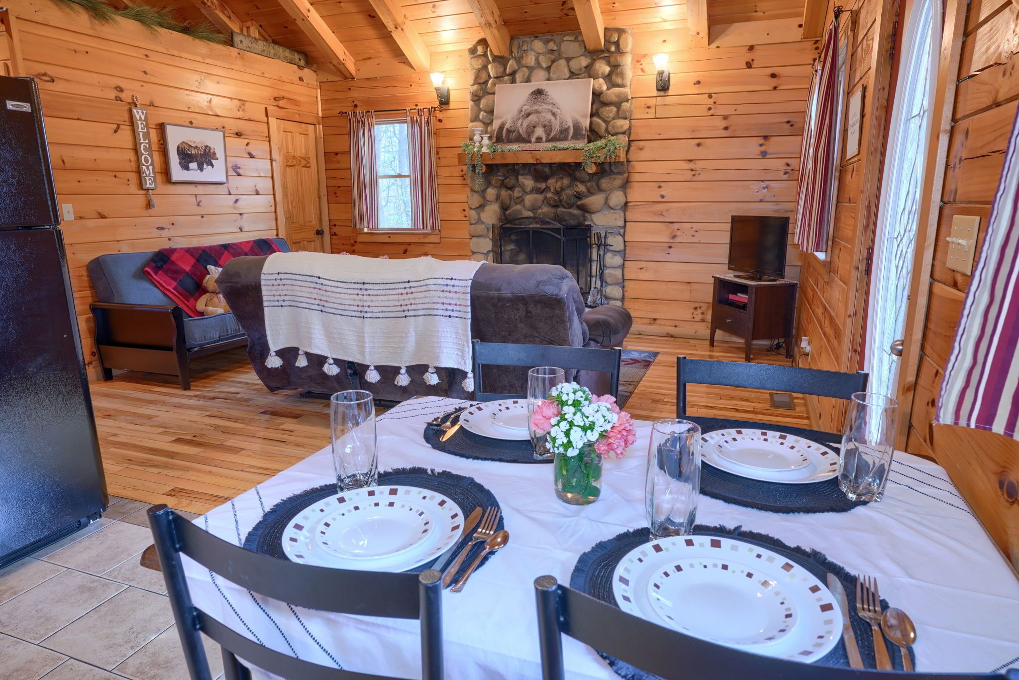 Ein gemütliches Blockhaus-Interieur mit einem Esstisch für vier Personen, einem Kamin und einer Wohnbereich mit Sofa und Decke.