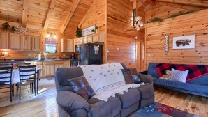 Ein gemütliches Blockhaus-Interieur mit Holzwänden, einem Essbereich, einer Couch und einer Küche.
