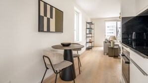 Une cuisine moderne avec un plan de travail noir, une table de salle à manger ronde surmontée d’un saladier et une bibliothèque.