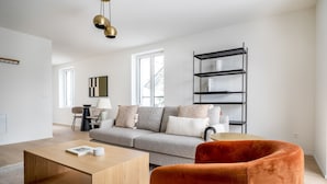 Un salon moderne avec un canapé gris, une table basse en bois et un fauteuil rouge. Un meuble de rangement noir est adossé au mur, et une lampe se trouve sur une table d’appoint.