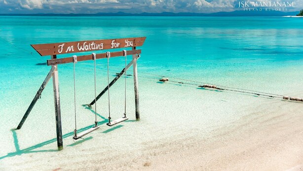 A wooden swing chair with a sign that reads "I'm Waiting for You" on a beach with clear turquoise water and a distant island. - JSK Mantanani Island Resorts Trademark by Wyndham (Kampung Mantanani)