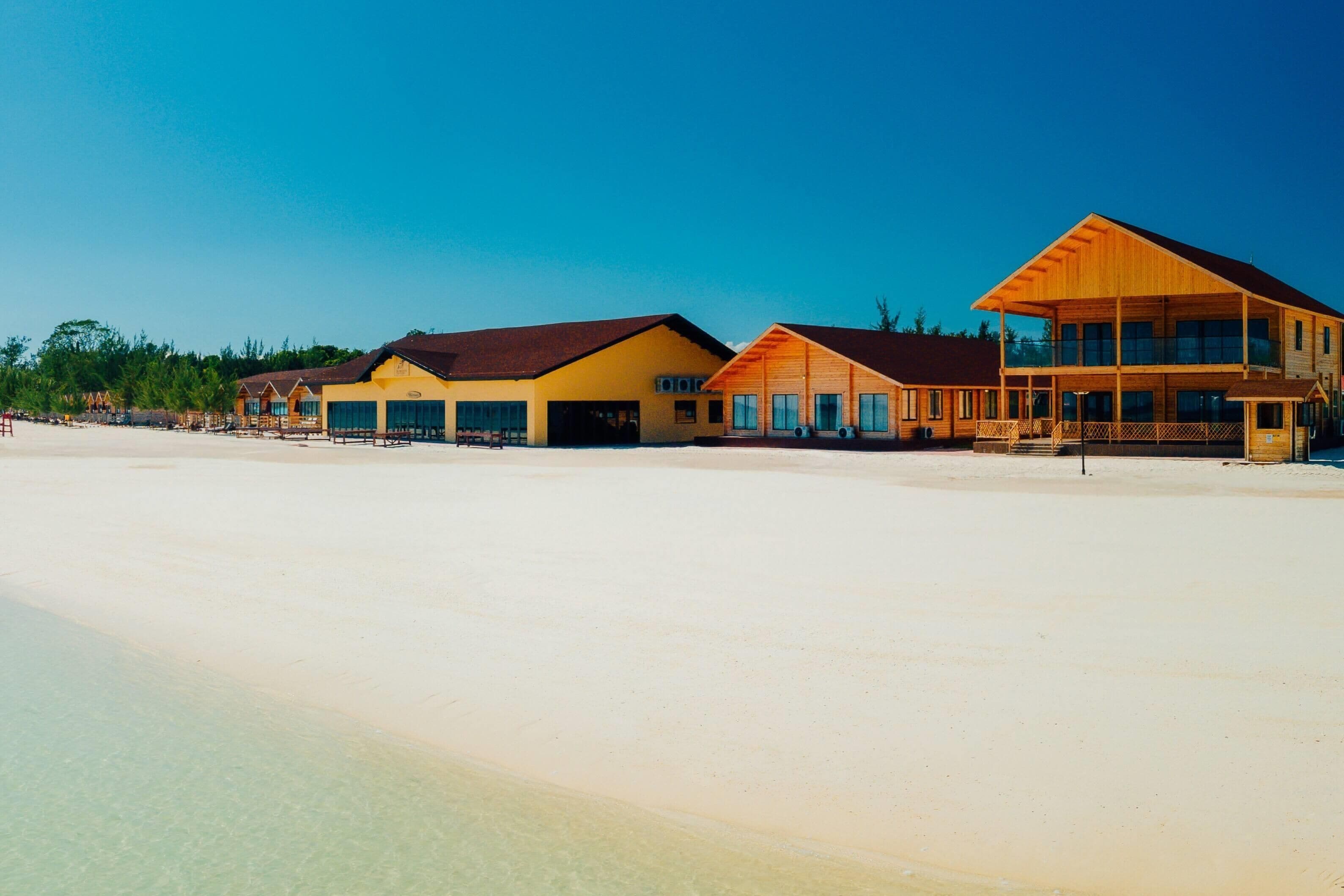 A beachfront hotel with multiple buildings, a sandy beach, and clear skies.