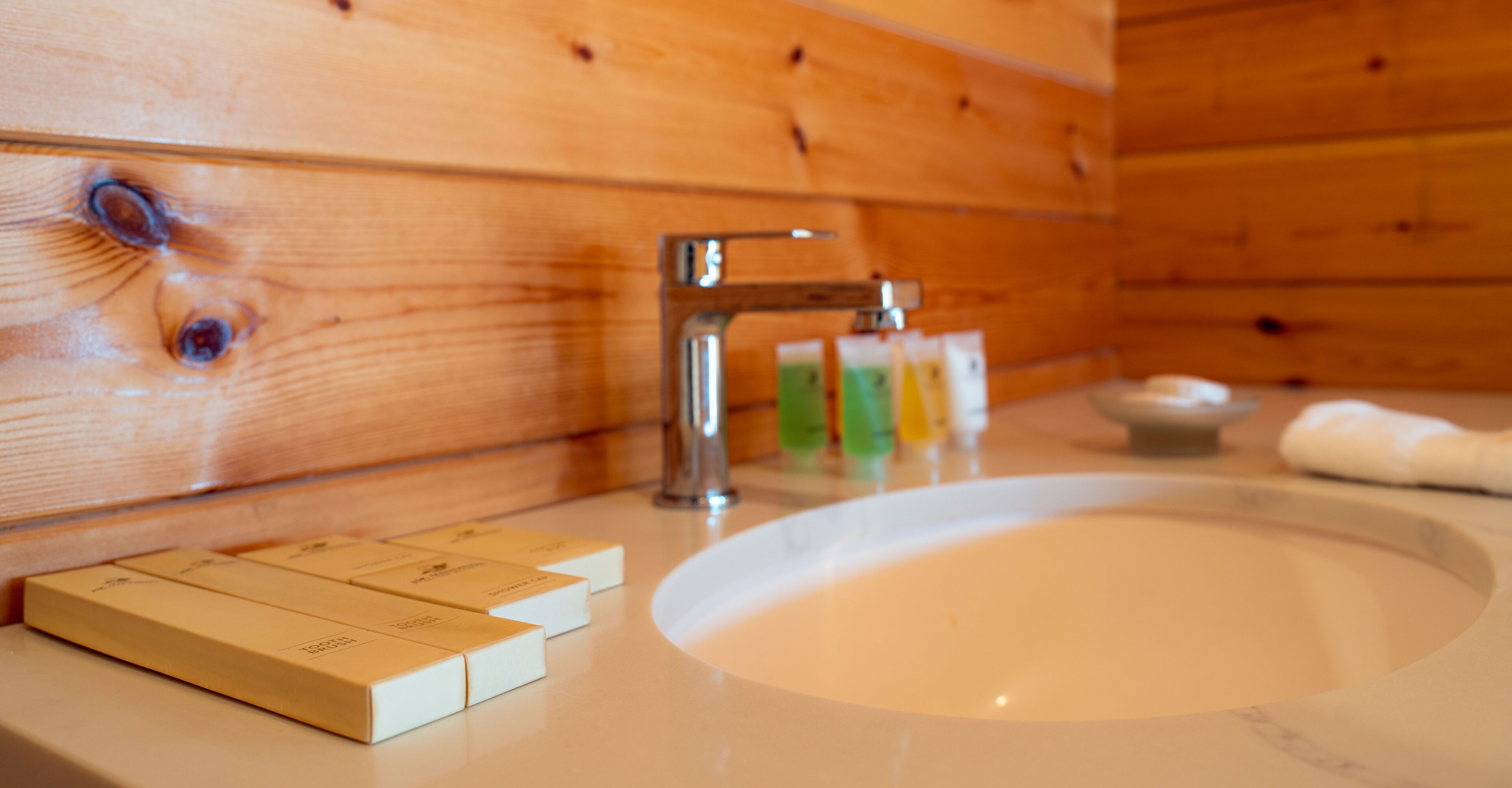 A wooden cabin interior with a bathroom sink, a faucet, and toiletries on the counter.