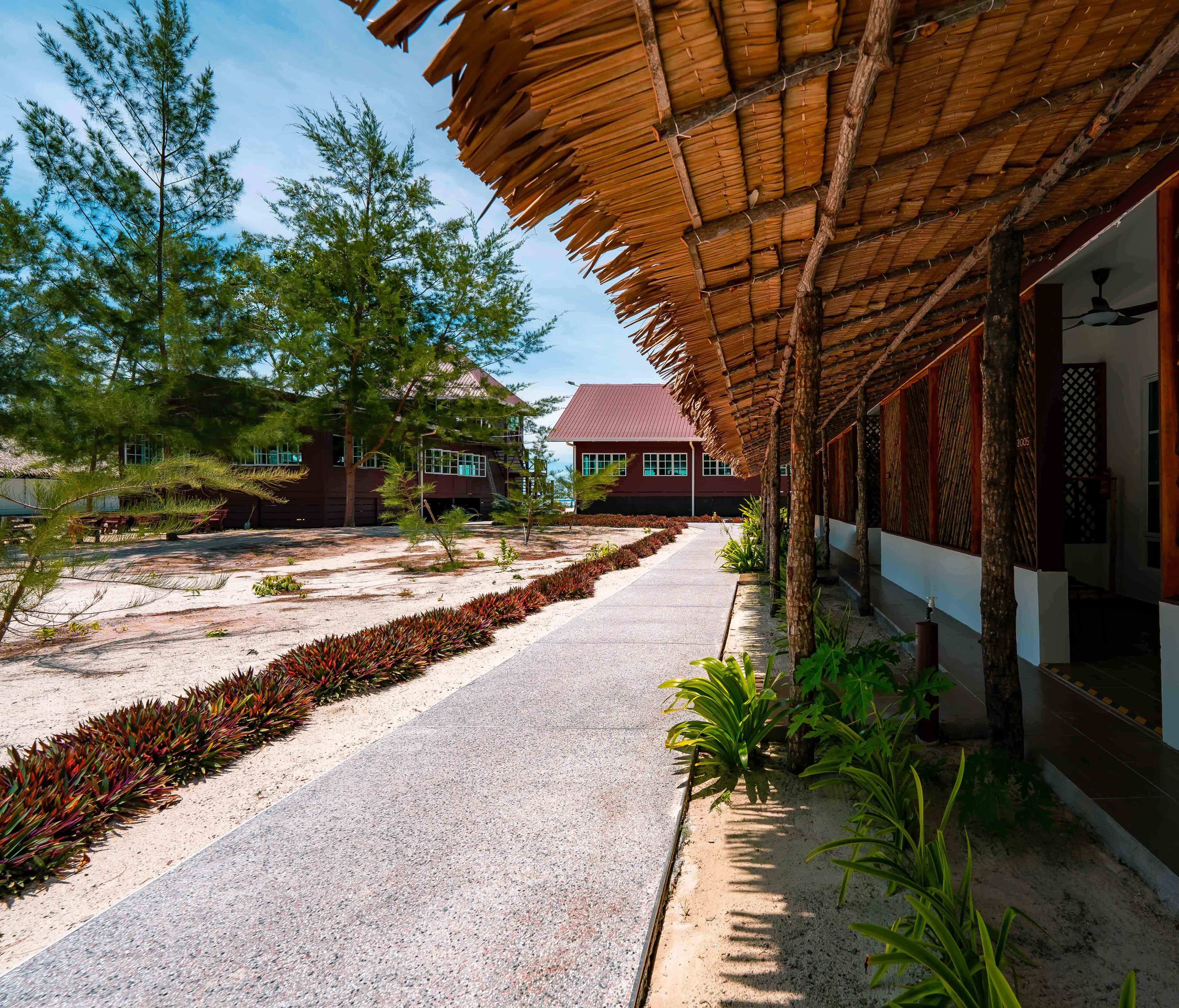 A covered walkway with a gravel path, surrounded by greenery and buildings with red roofs.