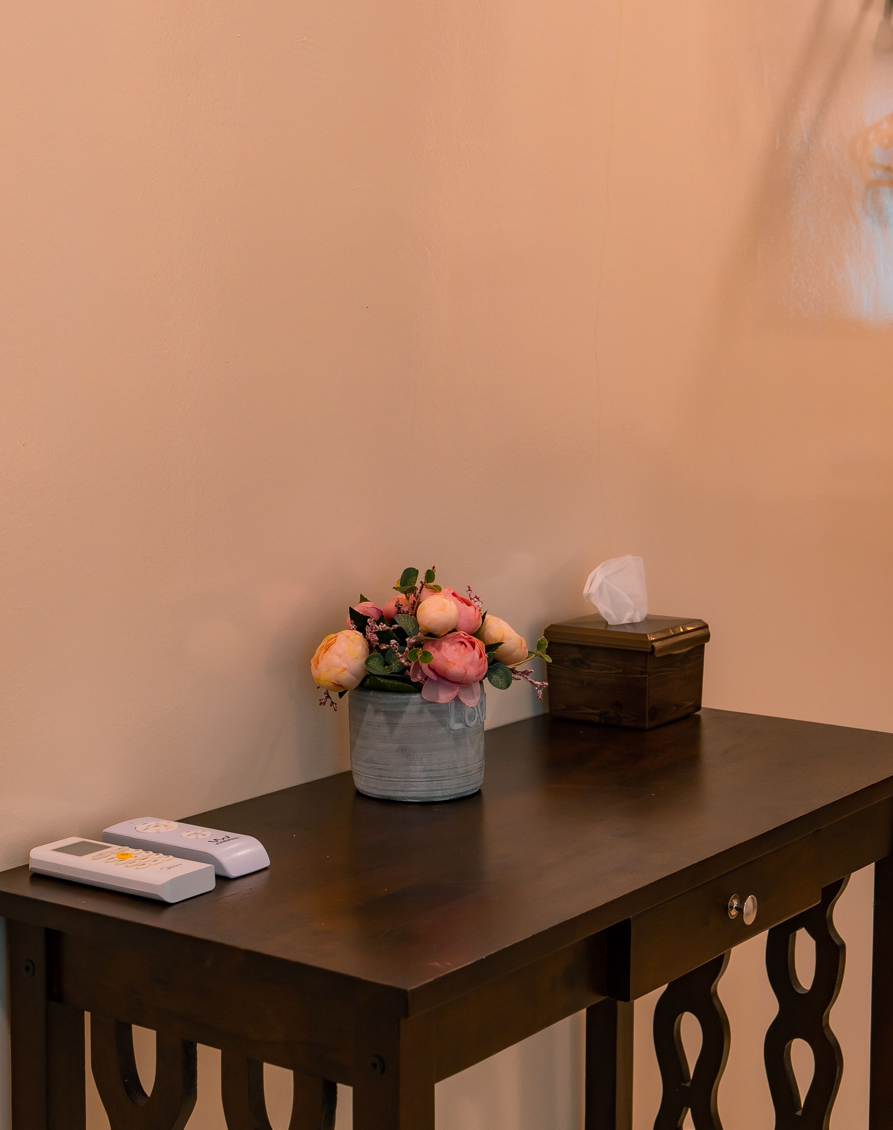 A wooden table with a vase of flowers, a tissue box, and a remote control.