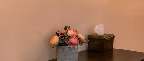 A wooden table with a vase of flowers, a tissue box, and a remote control.