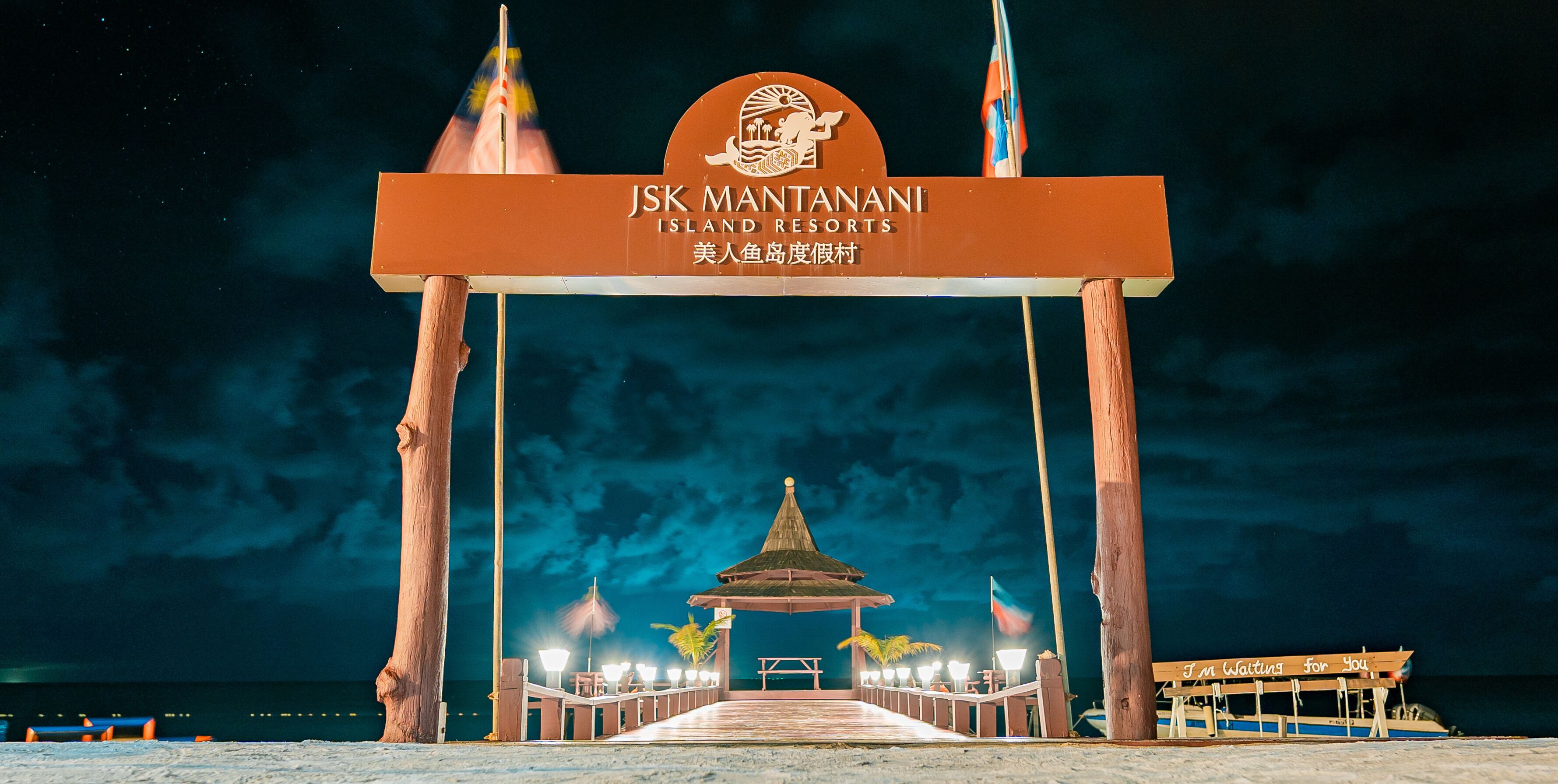 Un cartel de JSK Mantani Island Resorts con un pabellón tradicional y un barco amarrado en el muelle.