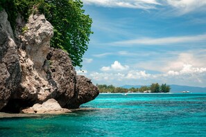 Un paysage côtier caractérisé par une falaise rocheuse, une eau turquoise et limpide, et une terre lointaine couverte de végétation.