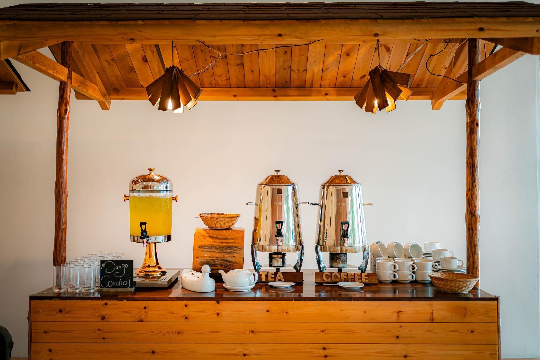 A coffee station with a wooden counter, two coffee makers, a tea maker, cups, and a teapot.