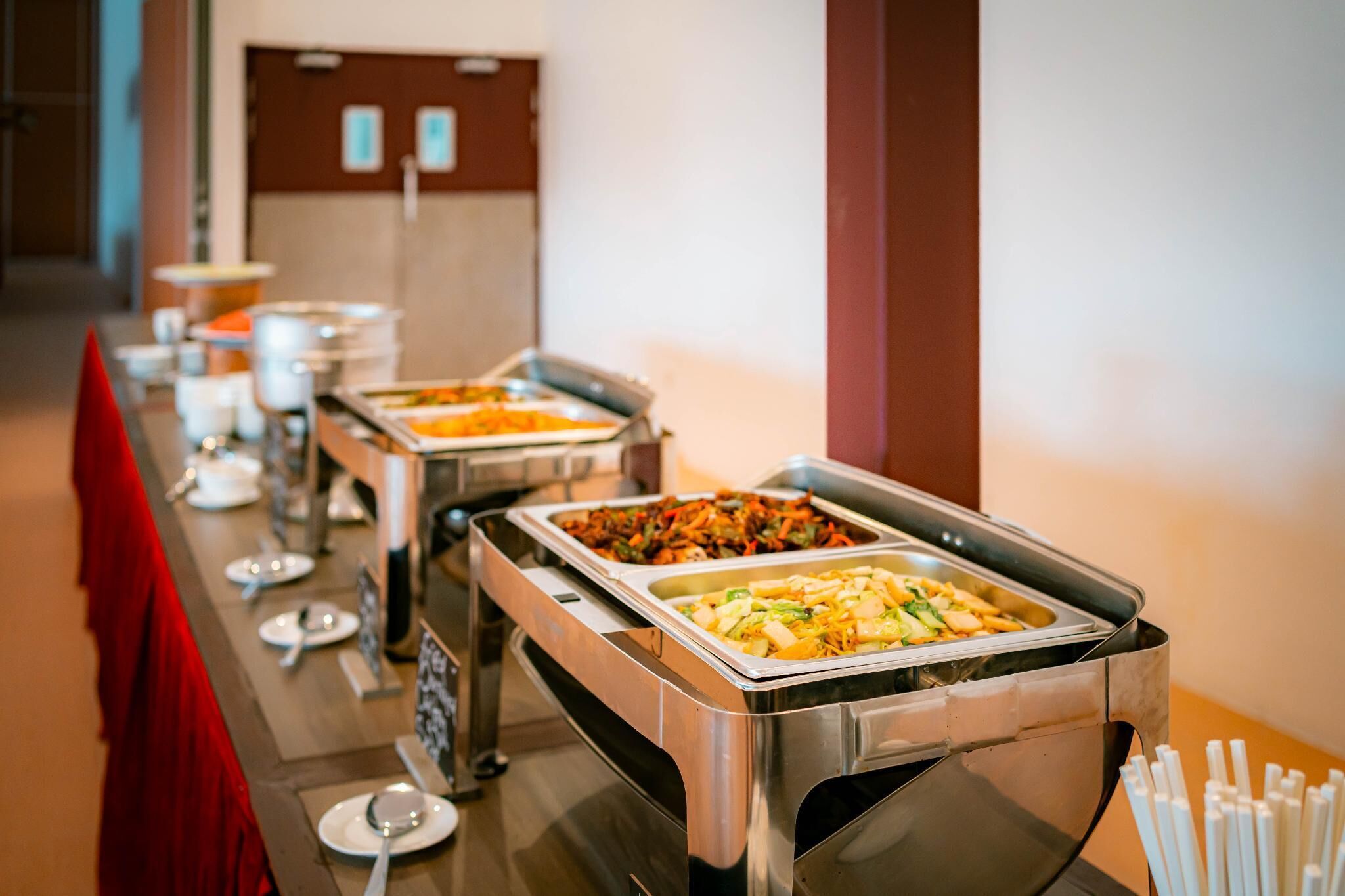 Un buffet proposant divers plats, une nappe rouge et une porte visible au fond.