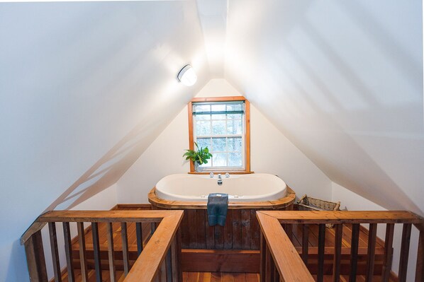 A small, triangular attic bedroom with a wooden staircase leading to a white bathtub.