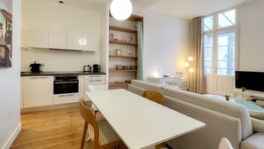 A modern apartment with a kitchen, dining area, and living room. It includes a white table, wooden chairs, a sofa, and a TV. - Superb apartment with Terrasse (Bordeaux)