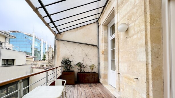 A wooden deck with a glass ceiling, white chairs, and potted plants. - Superb apartment with Terrasse (Bordeaux)