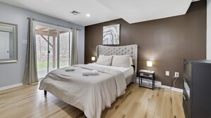 A bedroom with a large bed, a nightstand, a TV, and a window with curtains.