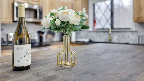 A bottle of wine and a vase with white flowers on a kitchen counter.