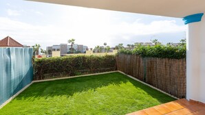 A backyard with a green lawn, a wooden fence, and a tiled patio. - CASA CARMEN - Wonderful apartment with shared pool and free WiFi. (Estepona)