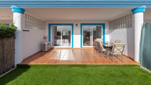 A patio with a dining table and chairs, a small air conditioning unit, and a green lawn. - CASA CARMEN - Wonderful apartment with shared pool and free WiFi. (Estepona)