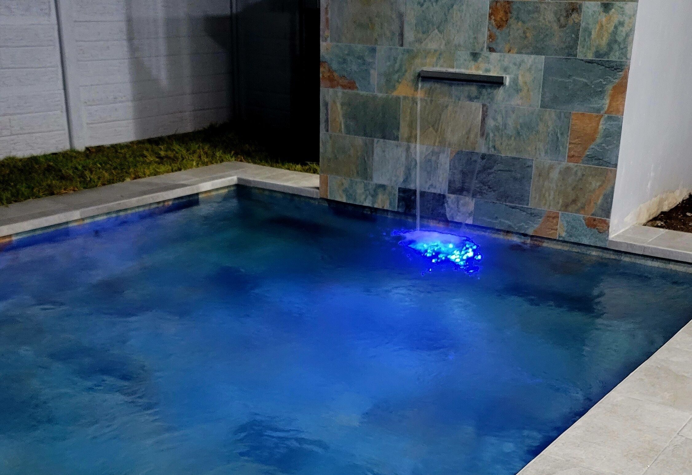 A swimming pool with a stone wall and a built-in water feature.