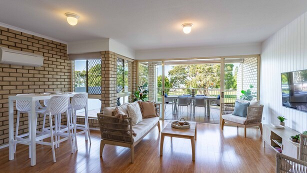 A spacious living area with a sofa, chairs, a coffee table, and a TV. There is a brick wall and a large window providing a view of the outdoors.