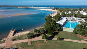 An aerial view of a coastal area with a swimming pool, beach, and clear blue waters.