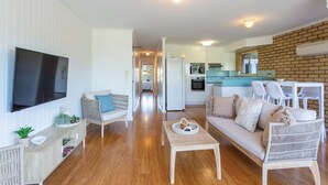 A modern living room with a flat-screen TV, wicker furniture, and a wooden coffee table.