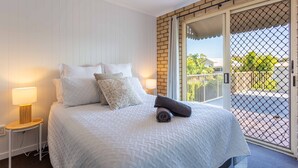 A hotel room with a bed, a nightstand, a lamp, a towel, and a view of the outside through a glass door.