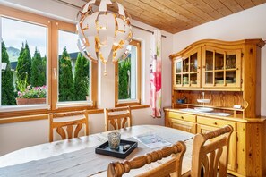 Een eetruimte met een houten tafel, stoelen, een kroonluchter en een houten kast met glazen deuren.