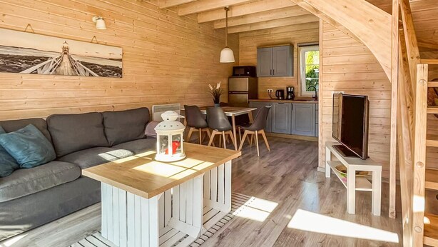 Un intérieur de chalet chaleureux comprenant un coin repas, une cuisine et un salon avec un canapé et une table.