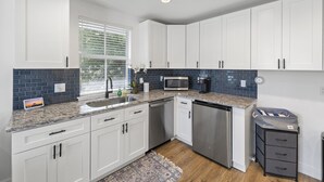 A modern kitchen with white cabinets, a granite countertop, a stainless steel dishwasher, and a coffee maker.