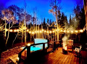 A wooden deck with a hot tub, surrounded by trees and string lights. - The Snow Shack 2BR w Hot Tub, Stream, Fireplace, Steam Rm on 5 Acres Near Breck (Alma)