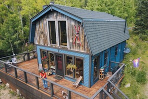A two-story wooden cabin with a deck, large windows, and a satellite dish. - The Snow Shack 2BR w Hot Tub, Stream, Fireplace, Steam Rm on 5 Acres Near Breck (Alma)