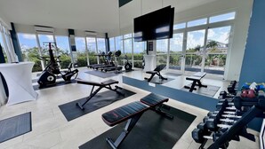 Une salle de sport moderne équipée de divers appareils d’exercice, dotée de grandes fenêtres et offrant une vue sur l’extérieur.