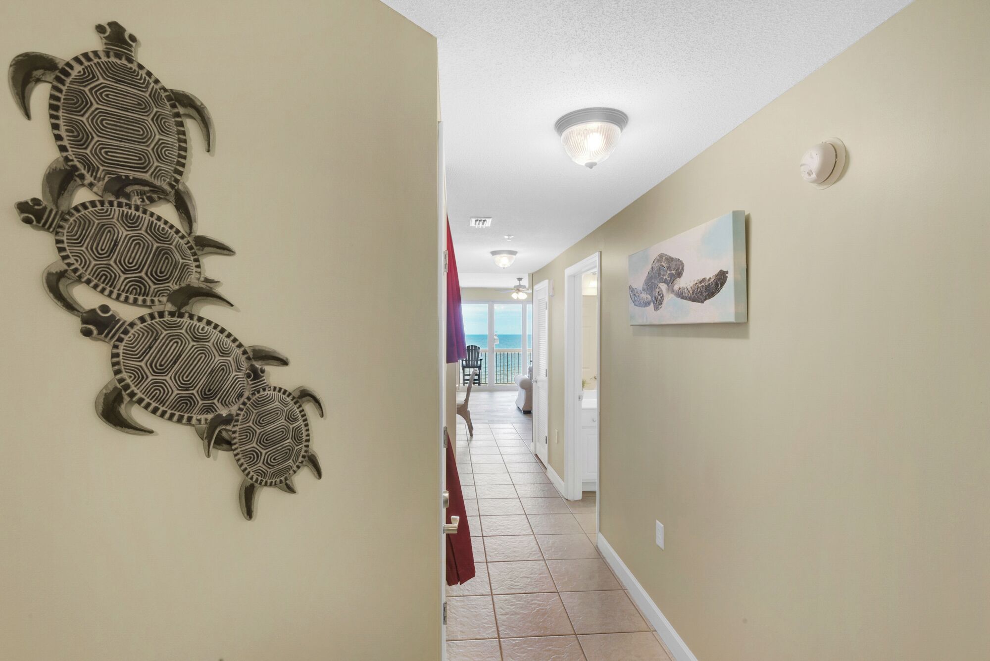 Ein Flur mit Wandkunst, die Schildkröten zeigt, einer Deckenleuchte und einer Tür zu einem Balkon mit Aussicht.