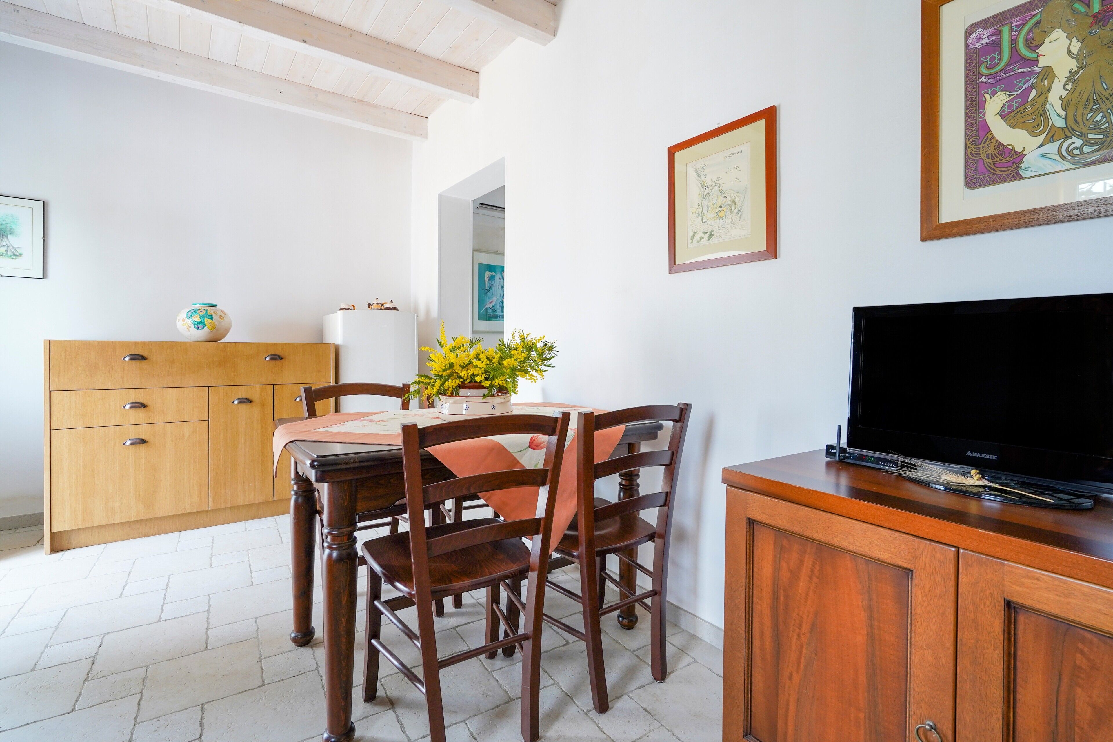 A dining area with a wooden table, chairs, a television on a cabinet, and artwork on the walls.
