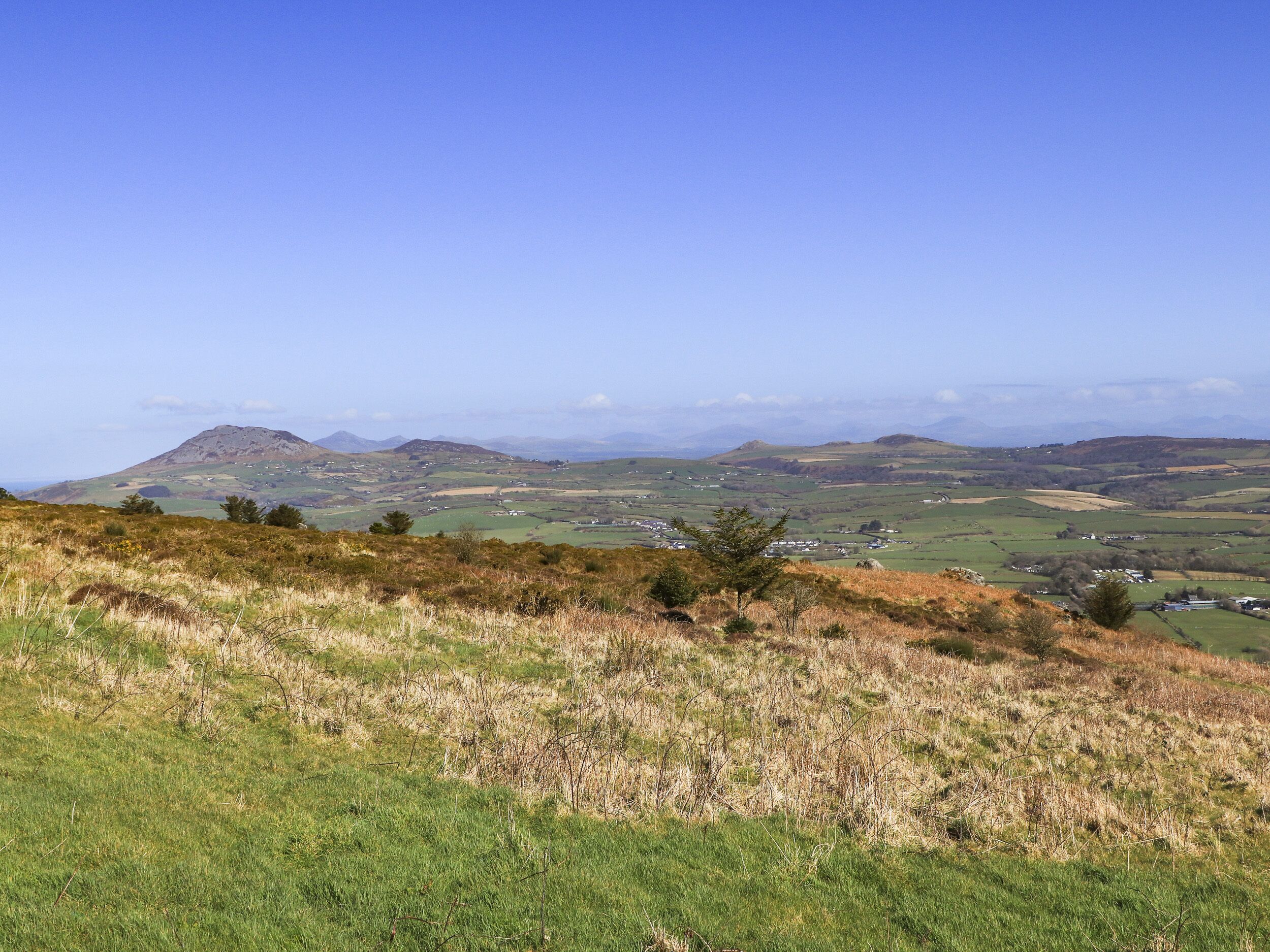 Ein weiter Panoramablick über eine hügelige Landschaft mit verstreuten Häusern und blauem Himmel.