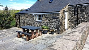 A stone building with a slate roof, a wooden bench, and potted plants. - Tir Eironwy (Pwllheli)