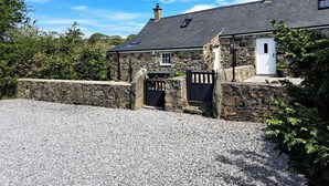 A stone building with a gravel driveway, a white door, and a stone wall. - Tir Eironwy (Pwllheli)