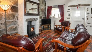 A cozy living room with a stone fireplace, leather furniture, and a television. - Tir Eironwy (Pwllheli)