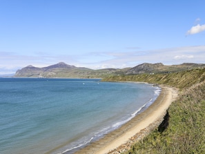 A coastal landscape with a sandy beach, clear blue water, and rolling hills in the background.