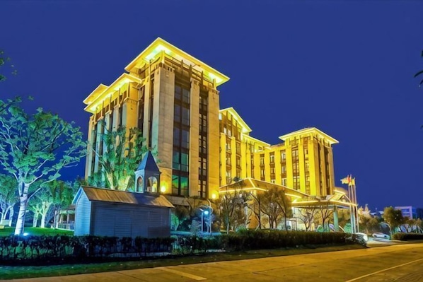 A large, multi-story hotel with a prominent central tower, a well-lit facade, and a landscaped front yard.