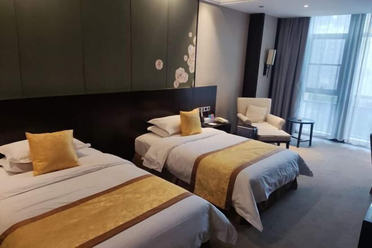 Een hotelkamer met twee bedden, een stoel, een klein tafeltje en een groot raam.