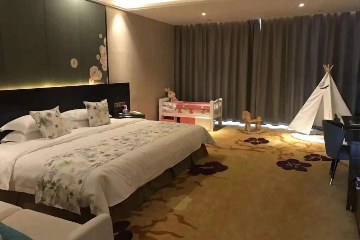 Hotelkamer met een groot bed, een bureau, een stoel, een witte tipi en een kleine speelhoek met een speelgoedpaard.