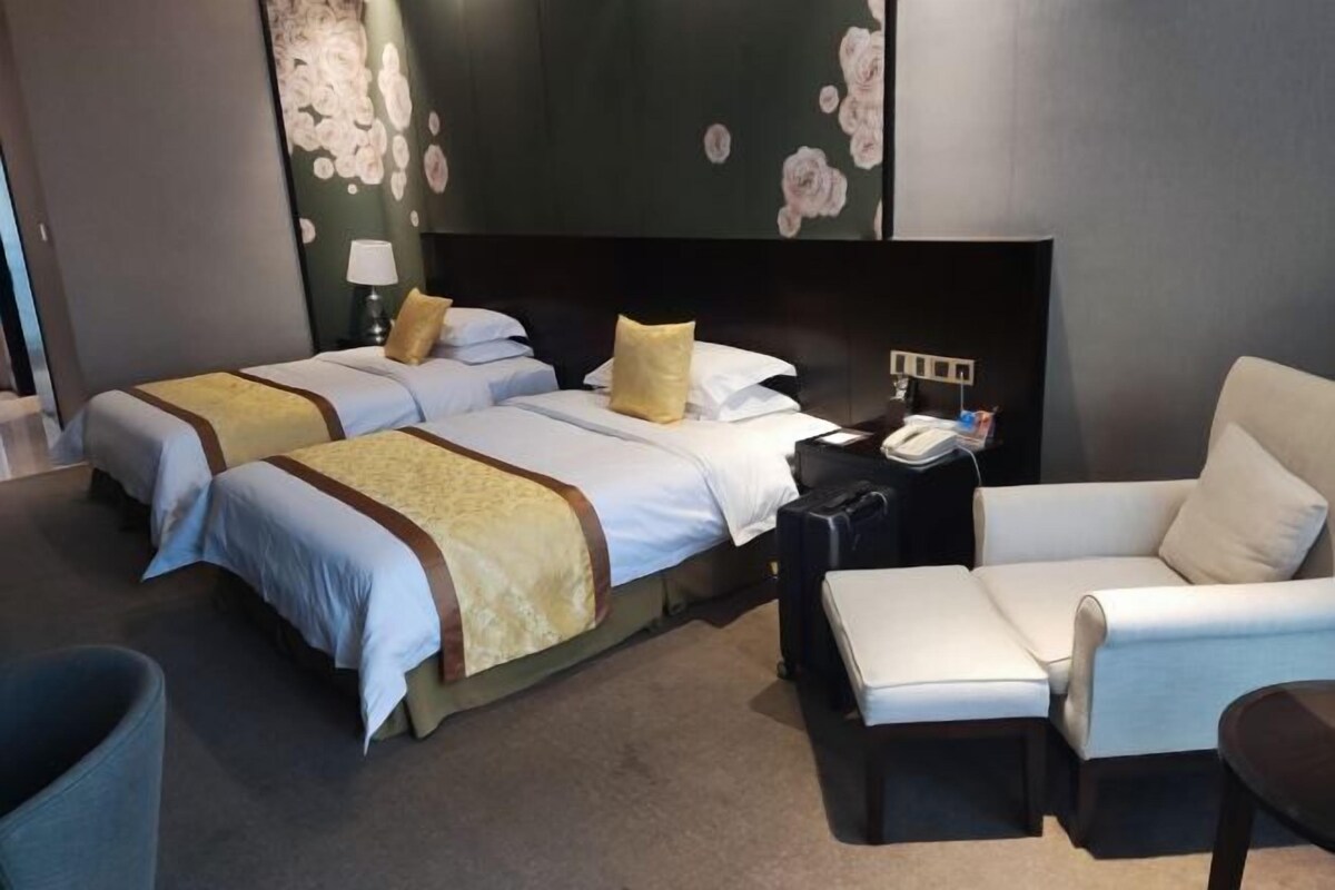 Quarto de hotel com duas camas, um sofá, uma escrivaninha com telefone e uma parede com papel de parede floral.