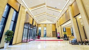 Un hall d’entrée spacieux avec un plafond haut, une moquette rouge et des plantes en pot.