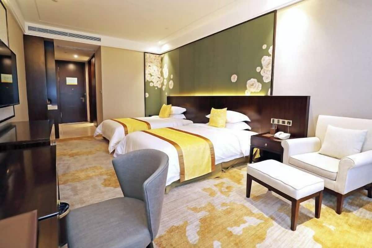Een hotelkamer met twee bedden, een bureau, een stoel, een bankje en een televisie.