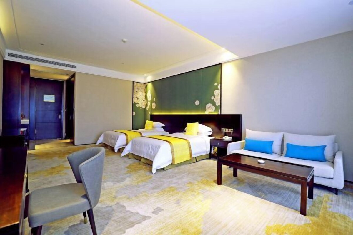 Quarto de hotel com duas camas, um sofá, uma escrivaninha e uma cadeira.