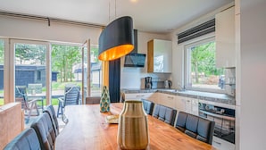 A modern kitchen with a dining area, featuring a wooden table, chairs, a vase, and a pendant light. - Wieringen Waddenlodge (Den Oever)