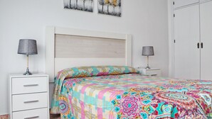 A bedroom with a bed, two bedside tables, a wardrobe, and two wall-mounted paintings.